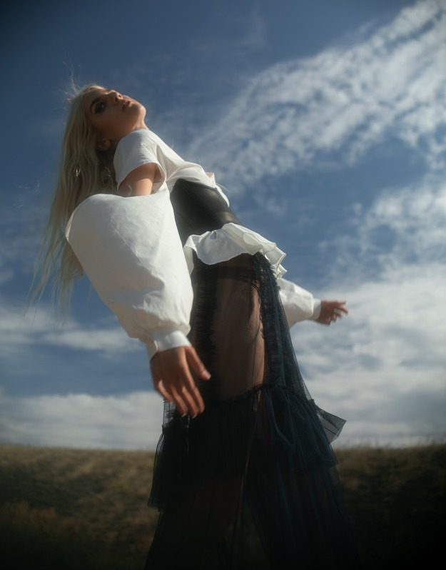 Model in a white blouse leaning back against the sky
